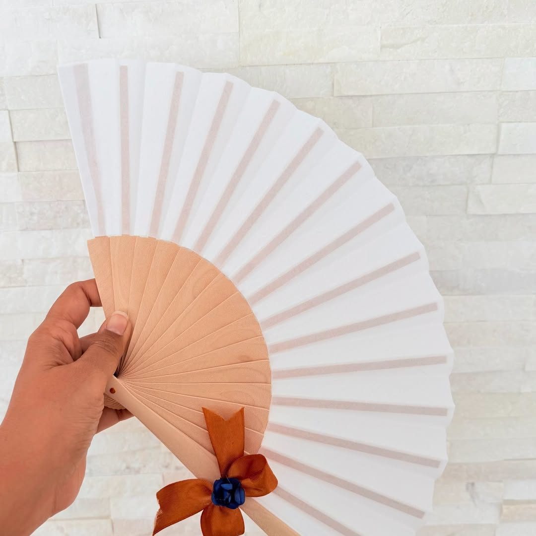 Éventail blanc à manche en bois, nœud satin orange et rose bleue, tenu à la main